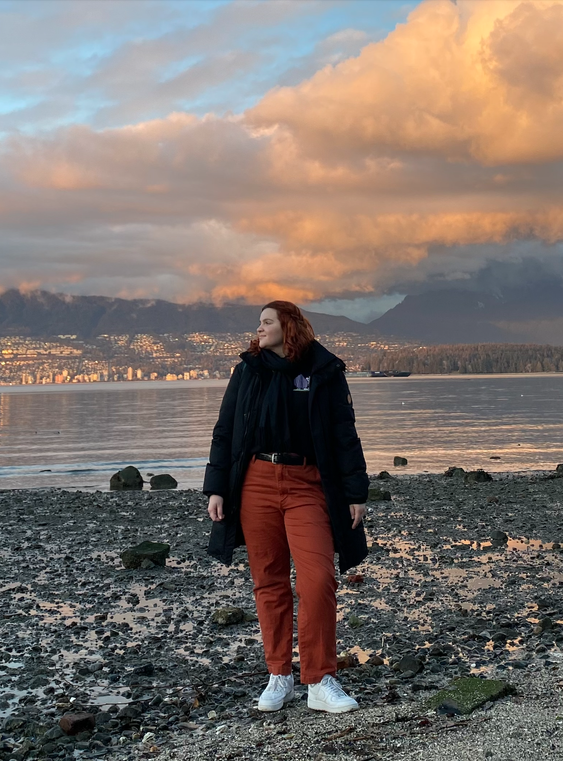 Author Valeriia Pelevina standing on a rocky beach under a cloudy sky